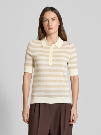 Frauenmodel trägt Regular Fit Poloshirt aus reiner Schurwolle Modell 'FIDENKA' von BOSS mit beigen und cremefarbenen Streifen, Feinstrick, Polokragen, gerippten Abschlüssen, Ganzkörperansicht von vorne.