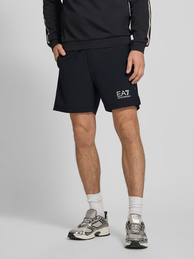 Männermodel trägt Shorts mit Logo und elastischem Bund von EA7 Emporio Armani, Schwarz, Regular Fit, Material-Mix, Nahaufnahme Unterkörper.