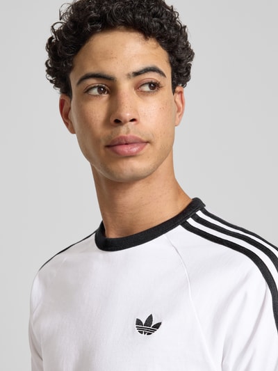 Männermodel trägt T-Shirt mit Label-Stitching von adidas Originals, weiß mit schwarzen Details, Baumwoll-Mix, Nahaufnahme Oberkörper.
