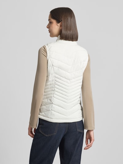 Vrouwenmodel draagt witte bodywarmer met opstaande kraag, model 'GS109' van G.I.G.A. DX, slim fit, ruglengte 61 cm, borstwijdte 49 cm, schouderbreedte 37 cm, waterdicht tot 10.000 mm, ritssluiting, ritszakken, ganzebody zicht van achteren.