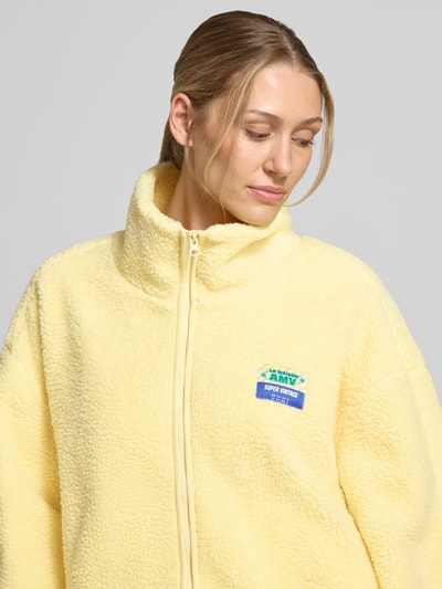 Frauenmodel trägt Oversized Jacke mit Stehkragen Modell 'Hoktown' von American Vintage in Hellgelb, Reißverschluss, Fleece-Textur, Nahaufnahme Oberkörper.
