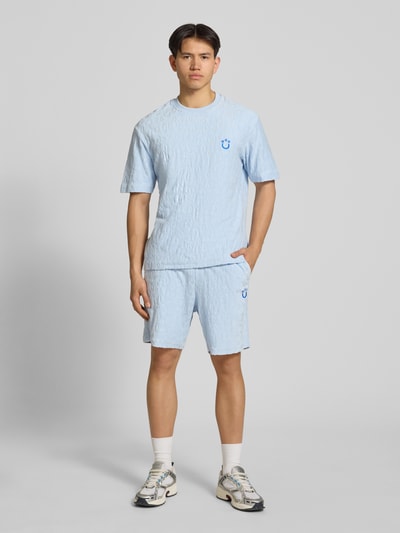 Męski model nosi Regular Fit Shorts aus Frottee od HUGO, imitacja froty, krój regular fit, wyhaftowane logo, tunel, wpuszczane kieszenie z przodu, nakładana kieszeń z tyłu, kolor jasnoniebieski, faktura froty, Ganzkörperansicht von vorne.
