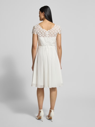 Vrouwenmodel draagt Cocktailkleid mit Rundhalsausschnitt und Perlen van Luxuar, wit, A-lijn, korte mouwen, ruglengte 80 cm, borstwijdte 38 cm, mouwlengte 13 cm, minijurk, detailrijke textuur met parels, volledige lichaamsaanzicht achterkant.