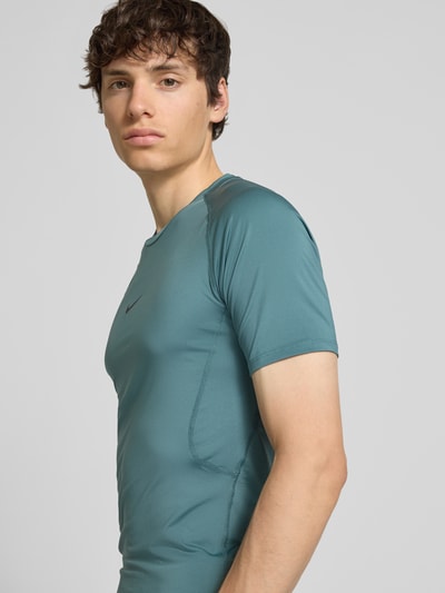 Männermodel trägt T-Shirt mit Logo-Print und Rundhalsausschnitt von NIKE TRAINING in Petrol, glatte Textur, Slim Fit, Nahaufnahme Oberkörper.