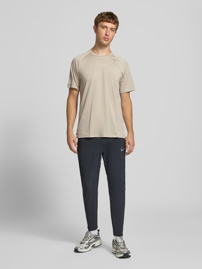 Männermodel trägt Regular Fit T-Shirt mit Aero-FIT-Technologie Modell 'STRIDE' von Nike, Herren Sport-T-Shirt, Beige und Grau, Ganzkörperansicht von vorne.