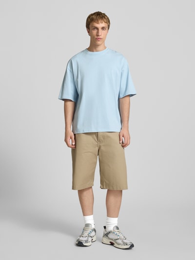 Męski model nosi Oversized T-Shirt mit Logo od REVIEW z czystej bawełny, jasnoniebieski kolor, krój oversized, okrągły dekolt, długość tyłu w rozmiarze M: 70 cm, widok całej sylwetki z przodu