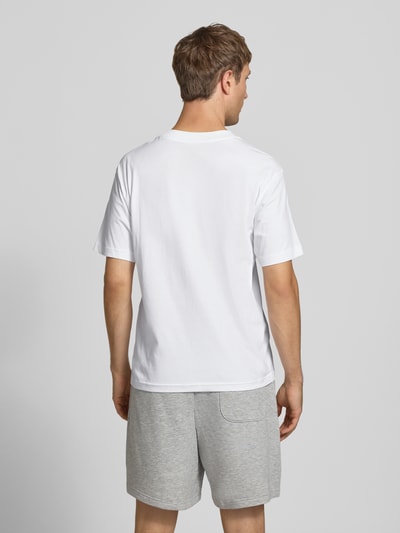 Männermodel trägt T-Shirt mit Label-Stitching Modell 'ESSENTIALS' von New Balance in Weiß, reine Baumwolle, gerade Form, Ganzkörperansicht Rückansicht.