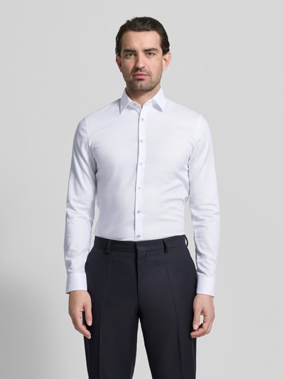 Męski model nosi Slim Fit Businesshemd mit Kentkragen od OLYMP No. Six, bawełna elastyczna, krój slim fit, zapięcie na guziki, długi rękaw, mankiety sportowe, długość pleców w rozmiarze 40: 81 cm, szerokość ramion w rozmiarze 40: 43 cm, długość rękawa w rozmiarze 40: 67 cm, biała, gładka struktura, widok całej sylwetki z przodu.