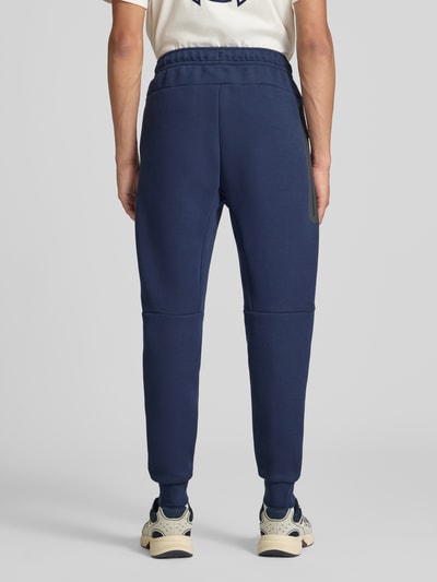 Mannenmodel draagt Slim Fit Sweathose uit katoenmix van Nike in donkerblauw met elastische tailleband, Heren Sweathose, volledige lichaamsweergave van achteren.