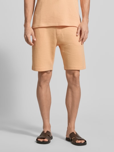 Männermodel trägt Regular Fit Shorts mit Tunnelzug von MCNEAL aus pfirsichfarbenem Baumwoll-Mix mit Stretch-Anteil, Eingrifftaschen, Gesäßtasche. Nahaufnahme Oberkörper bis Knie, Vorderansicht.