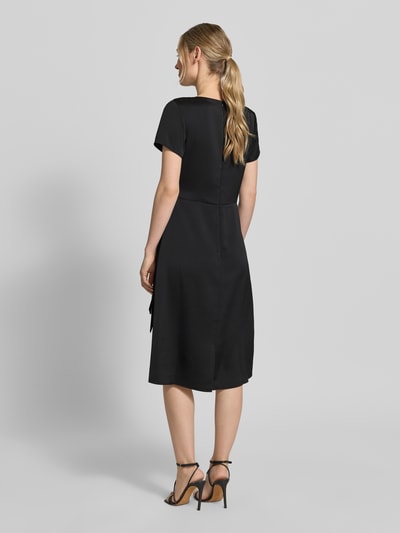 Frauenmodel trägt knielanges Cocktailkleid mit Knotendetail und Reißverschluss von Rinascimento in Schwarz, Taillierter Schnitt, glatte Textur, Knielänge, Rundhalsausschnitt, rückseitiger Reißverschluss, Rückenlänge 105 cm, Brustweite 46 cm, Ärmellänge 17 cm, Ganzkörperansicht Rückansicht.