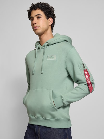Männermodel trägt Hoodie mit Känguru-Tasche von Alpha Industries in Mint, Baumwoll-Mix, Regular-Fit, Label-Patch, Nahaufnahme Oberkörper.