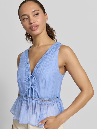 Frauenmodel trägt Top aus Lyocell-Mix mit Zierschleifen Modell 'Elena' von Mango in Hellblau, taillierte Passform, V-Ausschnitt, Loch-Stitching, ärmellos, strukturierte Textur, Nahaufnahme Oberkörper.
