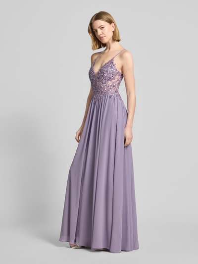Frauenmodel trägt Abendkleid mit Spitze und Strasssteinbesatz von Mascara aus Chiffon in Flieder, A-Linie, Maxikleid, V-Ausschnitt, Rückseitig überkreuzte Spaghettiträger, rückseitige Schnürung, Haken- und Reißverschluss, Rückenlänge 132 cm, Brustweite 40 cm, Ganzkörperansicht von vorne.