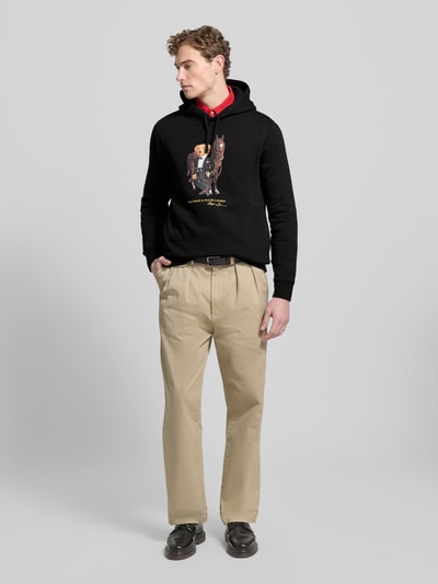 Mannelijk model draagt Hoodie met Label-Print van Polo Ralph Lauren in zwart, katoenmix, los model, capuchon, tunnelkoord, ribboorden, labelprint; ganzkörperansicht von voren.