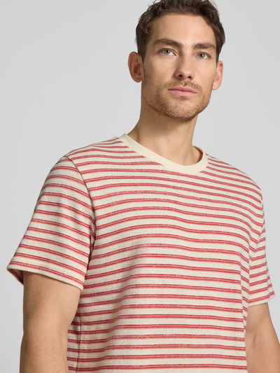 Männermodel trägt Regular Fit T-Shirt aus Baumwoll-Mix Modell 'KEVIN' von SELECTED HOMME, Optik: Allover-Muster, gestreift, Rundhals, Feinstrick, Farbkombination aus Creme und Rot, Kurzarm, Nahaufnahme Oberkörper.