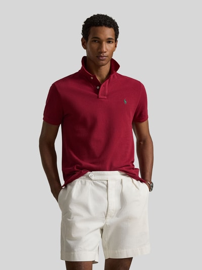 Mannenmodel draagt Regular Fit Poloshirt aus reiner Baumwolle van Polo Ralph Lauren in effen rood, piquétextuur, logodetail, polokraag, V-hals, korte knoopsluiting, korte mouwen met geribde zoom, zijsplitten, asymmetrische zoom, puur katoen, volledig lichaam van voren.
