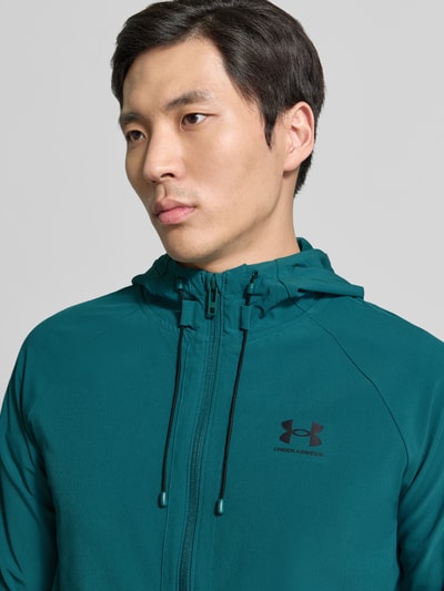 Männermodel trägt Regular Fit Jacke mit Logo-Print Modell 'Vibe' von Under Armour in Türkis, Kapuze, Reißverschluss, Nahaufnahme Oberkörper.