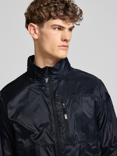 Männermodel trägt Regular Fit Jacke mit Stehkragen Modell 'Berg' von Ellesse in Schwarz mit Reißverschluss und Napoleontasche, Nahaufnahme Oberkörper.