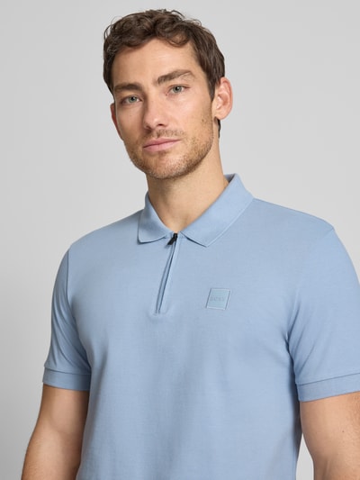 Männermodel trägt Slim Fit Poloshirt aus Baumwoll-Mix Modell 'PASSERZIP' von BOSS Orange, Optik: Unifarben, Label-Patch, Nahaufnahme Oberkörper.