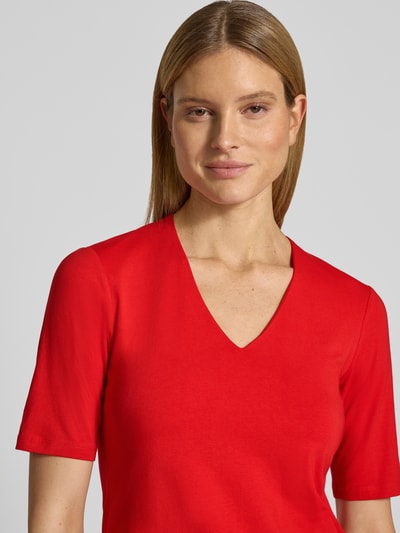 Vrouwenmodel draagt Regular Fit T-Shirt met V-hals van More & More in effen rood, katoenmix, met korte mouwen, ruglengte maat 36: 58 cm, close-up bovenlichaam.