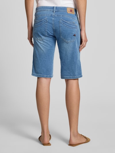 Frauenmodel trägt Jeansshorts mit asymmetrischem Knopfverschluss Modell 'Malibu' von Buena Vista aus Baumwoll-Mix mit Stretch-Anteil, Straight Fit, 5-Pocket-Design, blaue Waschung, sichtbare Struktur, Bundweite bei Größe S 36 cm, Innenbeinlänge bei Größe S 33 cm, Ganzkörperansicht Rückansicht.