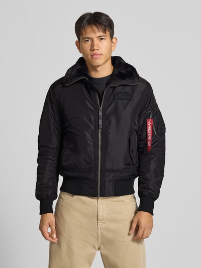 Männermodel trägt schwarze Bomberjacke mit Label-Patch und Kentkragen von Alpha Industries, sichtbare Eingrifftaschen, Ganzkörperansicht von vorne. Rückenlänge, Schulterbreite, Brustweite und Ärmellänge entsprechen Größe M.