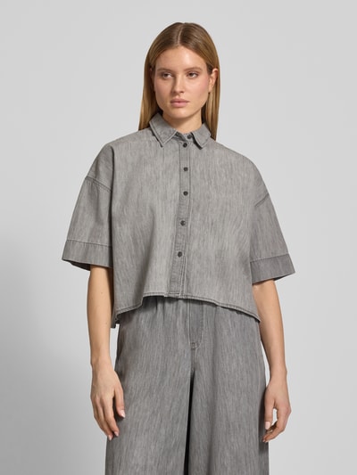 Modelka nosi bluzkę jeansową Boxy Fit Jeansbluse mit überschnittenen Schultern Modell 'YARIKA' od Drykorn z bawełny, szara, kołnierzyk koszulowy, listwa guzikowa, krótki rękaw, długość tyłu w rozmiarze 36: 53 cm, długość rękawów: 22 cm, pudełkowy krój, widok na cały korpus z przodu.