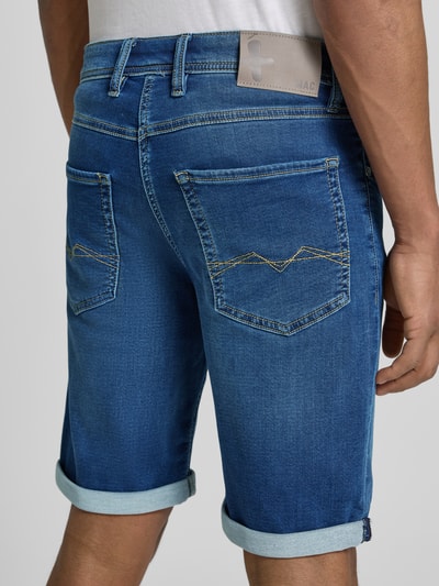 Mężczyzna nosi bermudy 'Bermudas in Denim-Optik' od MAC, tkanina stylizowana na denim, efekt znoszenia, szorty z wpuszczanymi kieszeniami, brzeg, krój regular fit, szerokość w rozmiarze 32: 44 cm, długość wewnętrzna nogawki: 25 cm, widok całej sylwetki z tyłu.