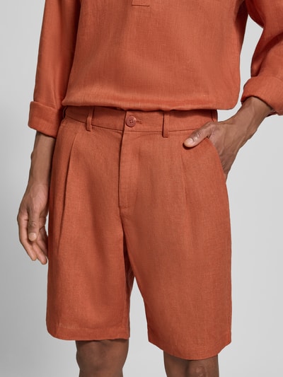 Männermodel trägt Bermudas aus reinem linnen von JAKE*S STUDIO MEN, los model, knoop- en ritssluiting, riemlussen, steek- en achterzakken, stolpplooi, kleur oranje, detailaufnahme.