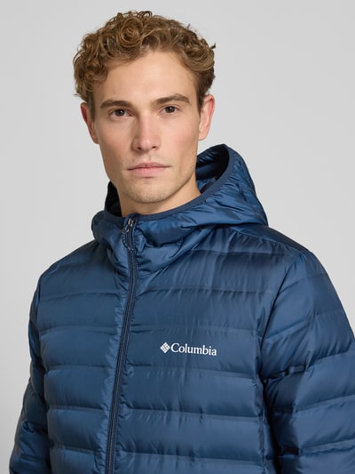 Mężczyzna nosi kurtkę pikowaną Regular Fit Model 'Lake 22™' od Columbia, kaptur, nadruk z logo, zamek błyskawiczny, niebieska, z efektem pikowania, zbliżenie na górną część ciała
