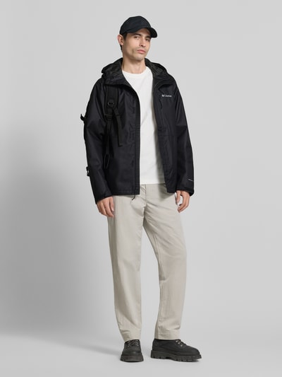 Męski model nosi kurtkę z kapturem model 'Hikebound™ II' od Columbia, krój regular fit, czarna, widoczne logo, patki przy mankietach, zamek błyskawiczny zakryty, całkowity widok z przodu