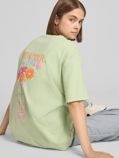 Frauenmodel trägt Oversized T-Shirt mit rückseitigem Print Modell 'Midsummer' von OH APRIL, reine Baumwolle, pastellgrün, Ganzkörperansicht Rückansicht.