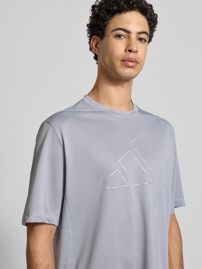 Männermodel trägt T-Shirt mit Label-Print von adidas Training in Hellgrau, Regular-Fit, Rundhalsausschnitt, Nahaufnahme Oberkörper, Rückenlänge 70 cm bei Größe M.