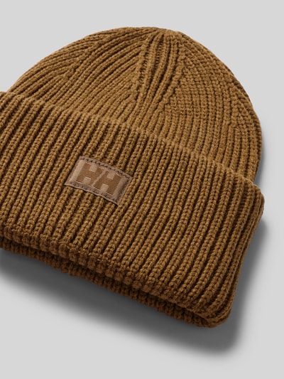 Produktfoto, Beanie in Strick-Optik mit Logo-Patch von Helly Hansen in Braun, Strukturmuster, fixierter Bund, nah vor grauem Hintergrund.