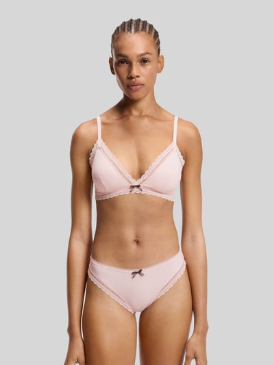 Frauenmodel trägt BH mit Spitzenbesatz Modell 'UNIQUE' von HUGO in zartem Rosa, Stretch-Material, Hakenverschluss, verstellbare Träger, Ganzkörperansicht von vorne.