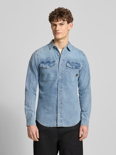Męski model nosi Slim Fit Freizeithemd aus reiner Baumwolle Modell 'Marine' von G-Star Raw, krój slim fit, kent kołnierzyk, listwa guzikowa, kieszenie na piersi, detal z logo, niebieski denim, długość tyłu w rozmiarze M: 75 cm, szerokość w rozmiarze M: 40 cm, długość rękawa w rozmiarze M: 67 cm, tekstura bawełny, widok całej sylwetki z przodu.
