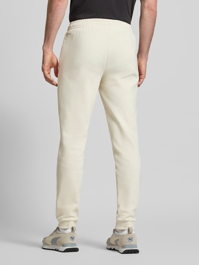 Männermodel trägt Regular Fit Sweathose mit Logo-Print Modell 'Pumatech' von PUMA PERFORMANCE aus Baumwoll-Mix in Creme, Ganzkörperansicht Rückansicht.