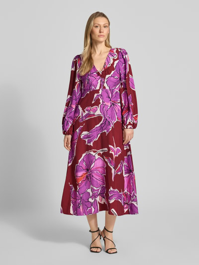 Frauenmodel trägt Midikleid aus Viskose-Mix mit V-Ausschnitt und Eingrifftaschen von Rich & Royal, florales Muster in Lila-Rot, Ganzkörperansicht von vorne, taillierter Schnitt, Leinen-Anteil, lange Ärmel, Raffungen, Reißverschluss hinten.