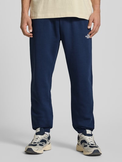 Männermodel trägt Sweatpants mit Logo-Print von The North Face in Dunkelblau, Baumwoll-Mix, Slim Fit, Nahaufnahme Unterkörper, Vorderansicht.