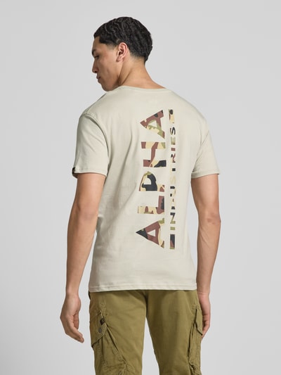 Männermodel trägt T-Shirt aus Baumwolle von Alpha Industries in Beige mit Label-Print-Details, Gerader-Schnitt, Ganzkörperansicht Rückansicht.