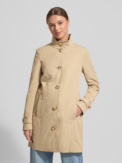Frauenmodel trägt Trenchcoat mit Stehkragen und Ärmelriegeln von Christian Berg Woman Selection in Beige, Knopfleiste, Ganzkörperansicht von vorne.