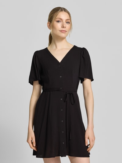 Frauenmodel trägt Leicht ausgestelltes Minikleid aus reiner Viskose Modell 'ALBA' von Vero Moda, Optik: Unifarben, Passform: Leicht ausgestellt, Mini-Länge, V-Ausschnitt, Taillengürtel, Knopfleiste, Kurzarm, Weite Ärmel, Material: Reine Viskose, Nahaufnahme Oberkörper.