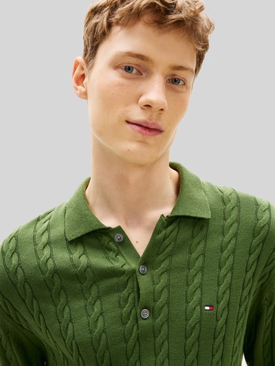 Männermodel trägt Regular Fit Strickpullover aus reiner Baumwolle von Tommy Hilfiger in grün mit Zopfmuster, Nahaufnahme Oberkörper.