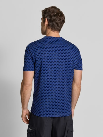 Męski model trägt Regular Fit T-Shirt mit Allover-Print von Armani Exchange, okrągły dekolt, krój regular fit, nadruk na całej powierzchni, z krótkim rękawem, Długość tyłu w rozmiarze M: 63 cm, Ganzkörperansicht Rückansicht.