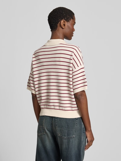 Frauenmodel trägt Relaxed Poloshirt mit Woll-Anteil von ROTATE im creme-roten Streifenmuster, Strick-Optik, Modal-Mix, Relaxed-Fit, Polokragen, kurzärmelig, Rückenlänge 52 cm bei Größe S, Ganzkörperansicht Rückansicht.