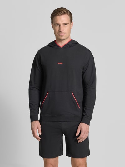 Männermodel trägt Regular Fit Hoodie aus Baumwoll-Mix Modell 'NOAH' von HUGO in Schwarz mit roten Details, Ganzkörperansicht von vorne, Herren T-Shirt von HUGO.