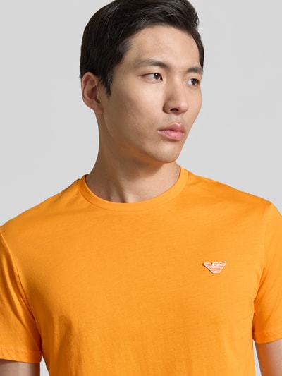Männermodel trägt T-Shirt mit Logo-Patch und Rundhalsausschnitt von Emporio Armani in Orange, Reine Baumwolle, Modern Fit, Nahaufnahme Oberkörper. Rückenlänge bei Größe M: 69 cm.