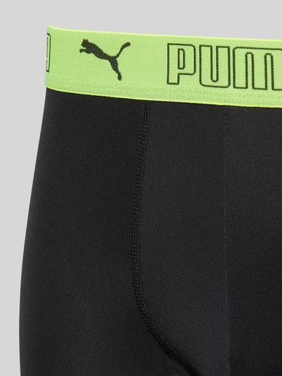 Männermodel trägt Slim Fit Trunk mit Logo-Stitching von PUMA, schwarzer Elastischer-Material-Mix, neongrüner Elastischer-Logo-Bund, Nahaufnahme Vorderansicht.