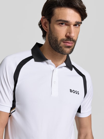 Męski model nosi Slim Fit Poloshirt mit kurzer Knopfleiste Modell 'PL_TOC SPIN CB' von BOSS Green, efekt: jednolity kolor, krój slim fit, nadruk z logo, kołnierzyk polo, zapięcie: krótka listwa guzikowa, rękaw: krótki rękaw, wykończenie materiału: dżersej, zbliżenie na górną część ciała.